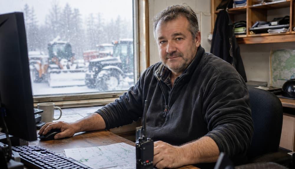 A contractor owner at his dispatch desk, his plows working outside the window